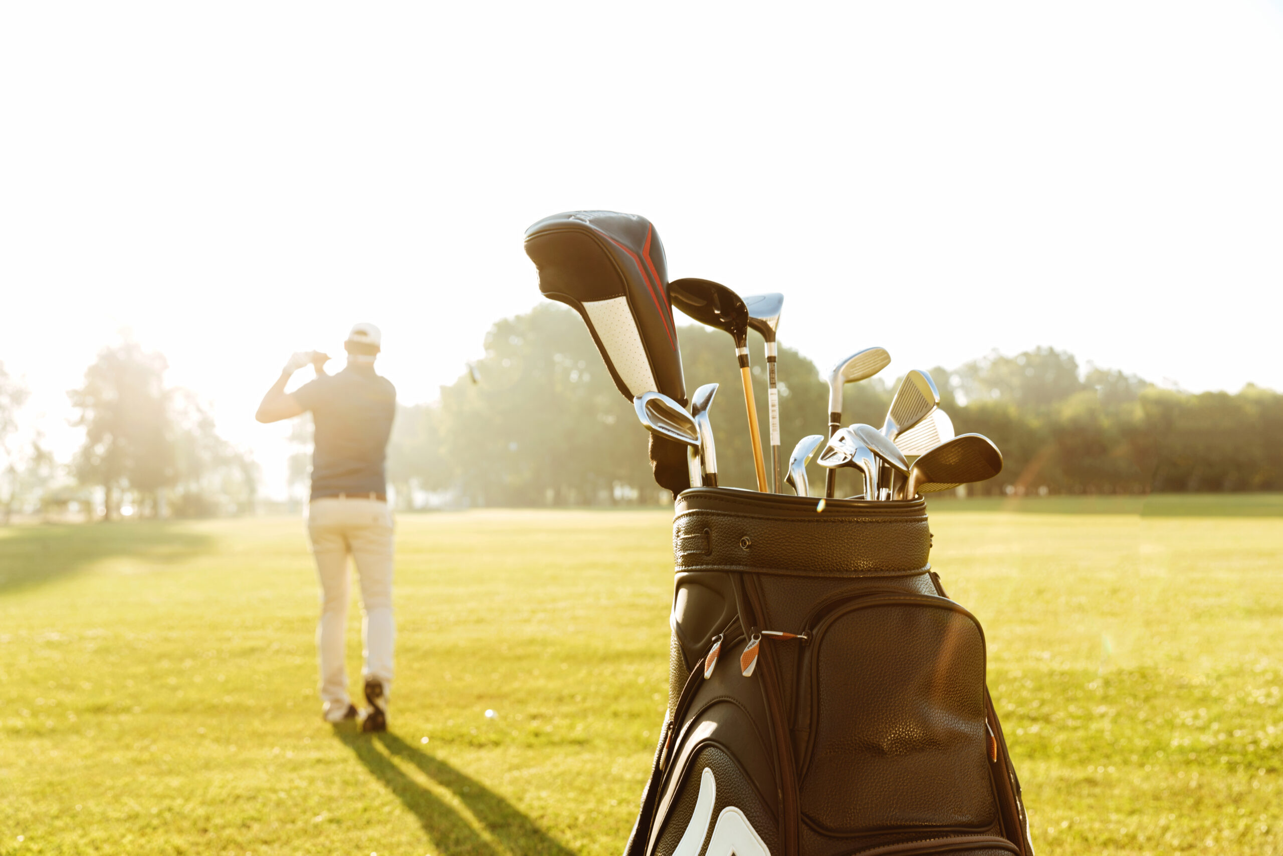 Back view of a male golfer swinging golf club and following shot in the air